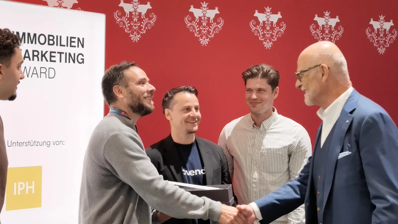 Händedruck bei der Preisverleihung: das avendo-Team mit Gratulanten vor der roten Wand und dem Banner des Immobilien-Marketing-Award